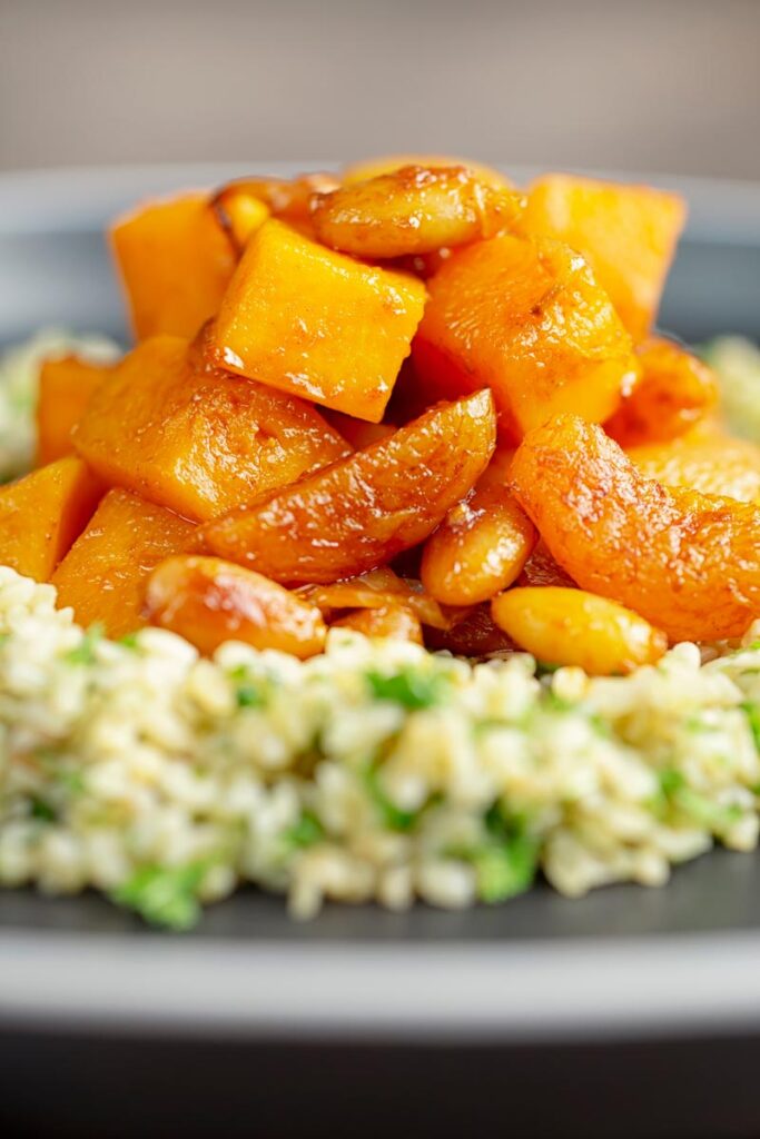 Portrait close up image of a butternut squash tagine with dried apricots and almonds served on a bed of herbed bulgur wheat