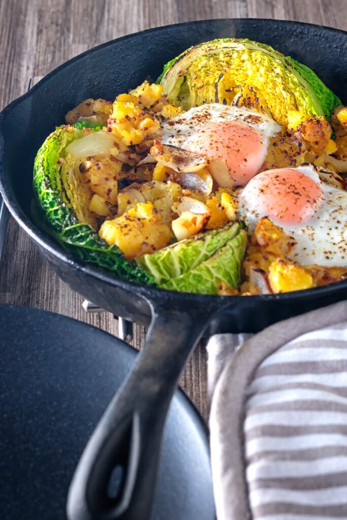 Portrait image of a cabbage and potato bake with eggs cooked and served in a cast iron skillet