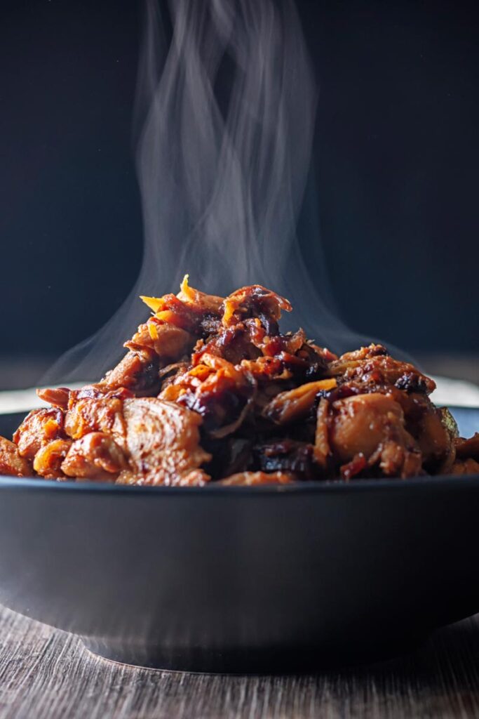 Portrait close up image of a steaming black bowl of chicken pickle or achari chicken.