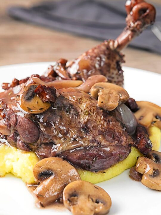 Portrait image of chicken in a red wine sauce with mushrooms and bacon served on mashed potato