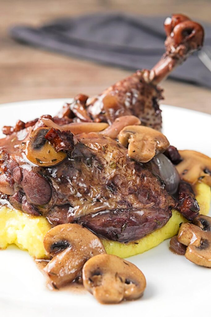 Portrait image of chicken in a red wine sauce with mushrooms and bacon served on mashed potato
