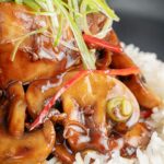 Portrait close up image of a Chinese chicken and mushroom stir fry served with shredded spring onion and white rice