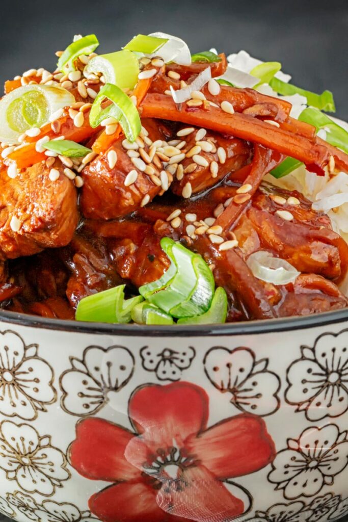 Portrait close up image of a Chinese orange chicken stir fry garnished with sesame seeds and spring onions