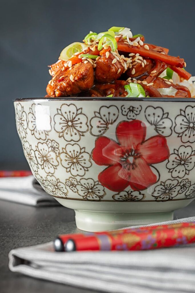 Portrait image of a Chinese orange chicken stir fry garnished with sesame seeds and spring onions