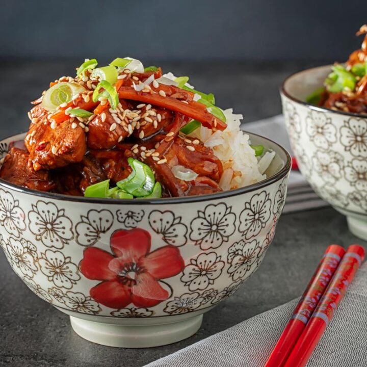 Square image of a Chinese orange chicken stir fry garnished with sesame seeds and spring onions