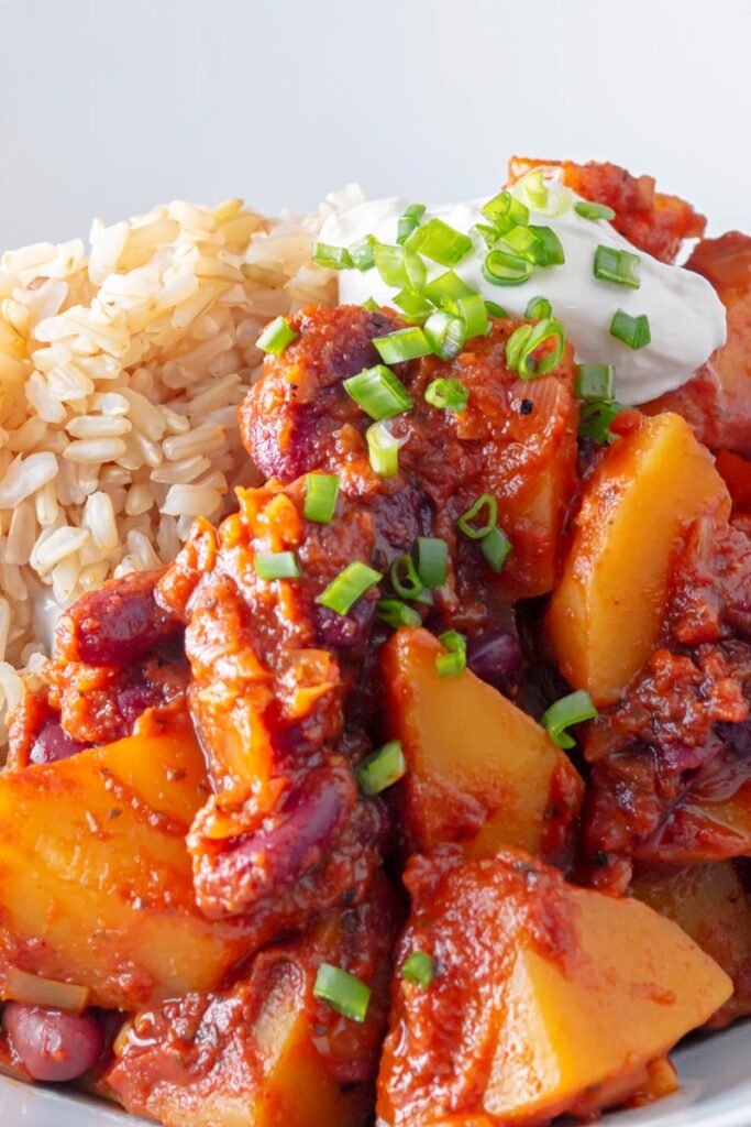 Portrait image of a butternut squash chili served with snipped chives and a dollop of sour cream in a white bowl