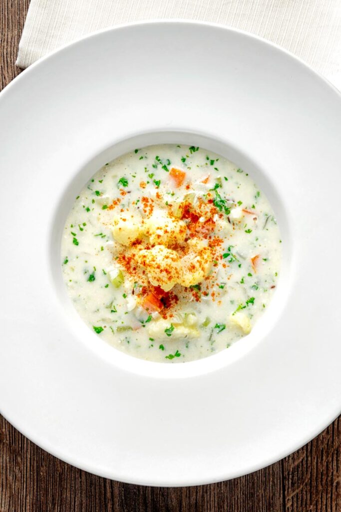Portrait overhead image of cauliflower florets ina cream of cauliflower soup with flecks of parsley and paprika