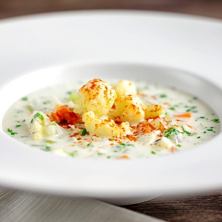 Square image of cauliflower florets in a cream of cauliflower soup with flecks of parsley and paprika