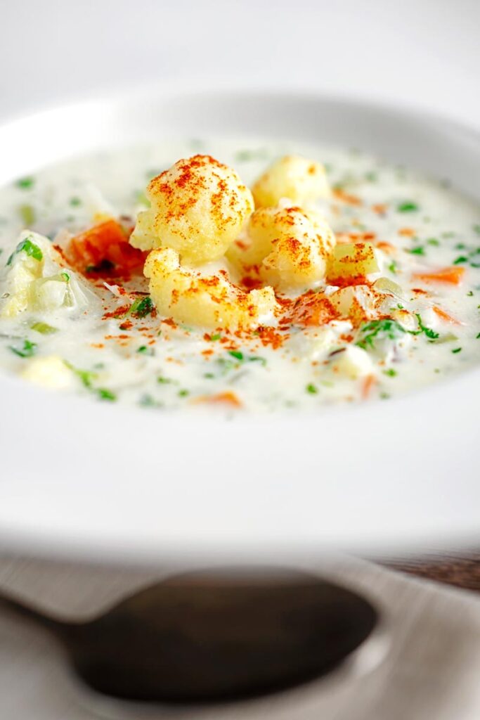 Portrait image of cauliflower florets in a cream of cauliflower soup with flecks of parsley and paprika