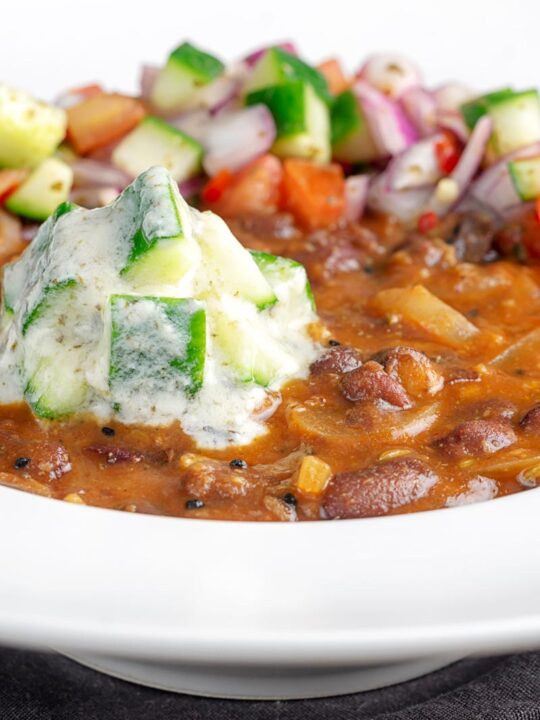 Portrait image of cucumber and mint raita served on a rakma masala kidny bean curry in a white bowl