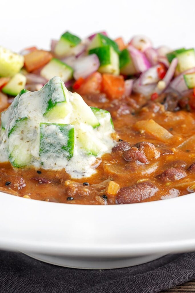 Portrait image of cucumber and mint raita served on a rakma masala kidny bean curry in a white bowl