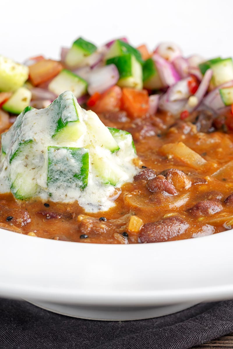 Portrait image of cucumber and mint raita served on a rakma masala kidny bean curry in a white bowl