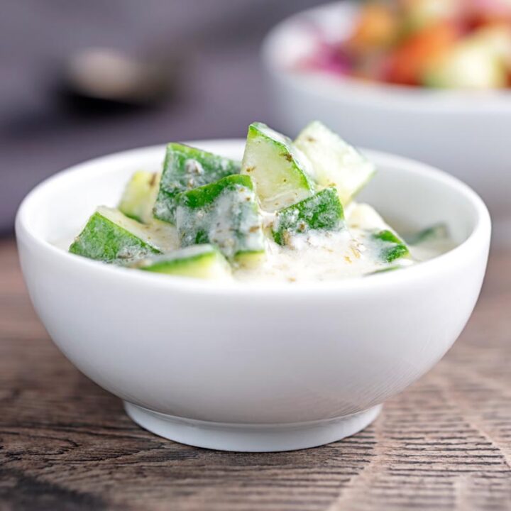 Square image of a cucumber and mint raita served in a small white bowl