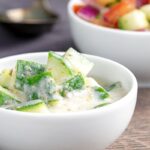 Portrait image of a cucumber and mint raita served in a small white bowl.