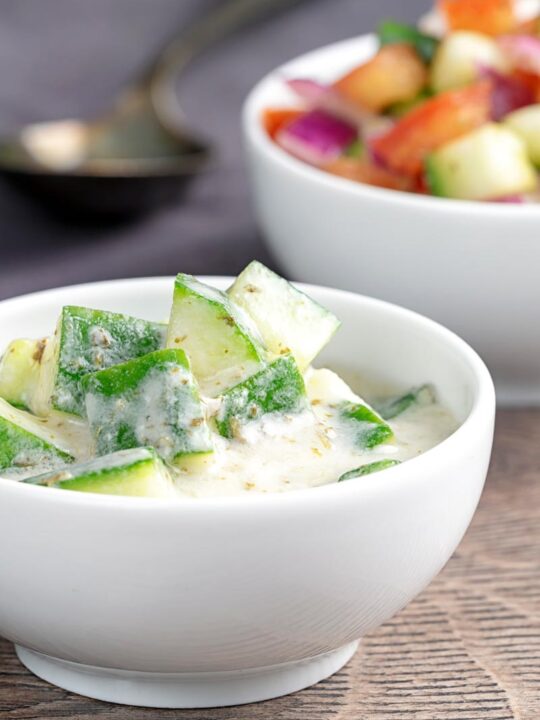 Portrait image of a cucumber and mint raita served in a small white bowl.