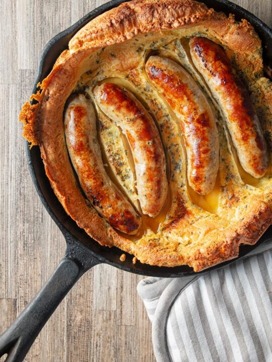 Portrait overhead image of toad in the hole, or sausages cooked in a Yorkshire pudding batter cooked and served in a cast iron skillet
