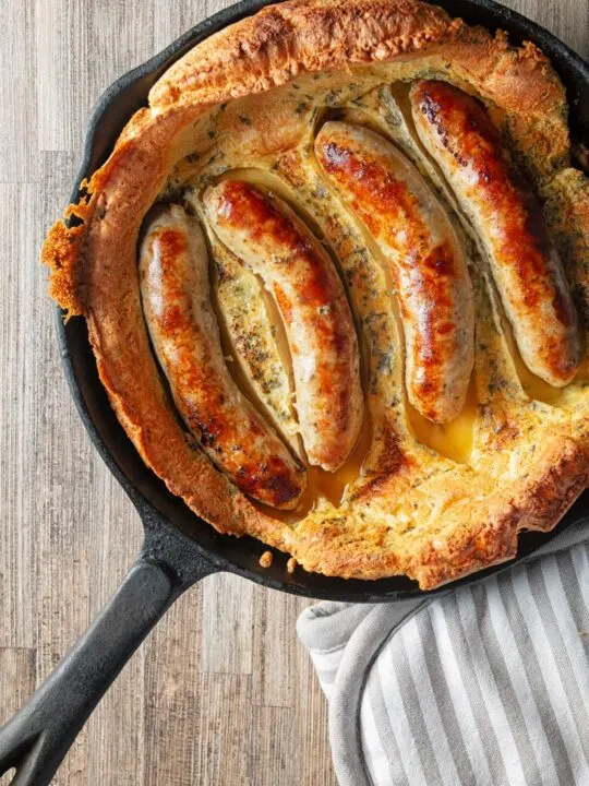 Portrait overhead image of toad in the hole, or sausages cooked in a Yorkshire pudding batter cooked and served in a cast iron skillet
