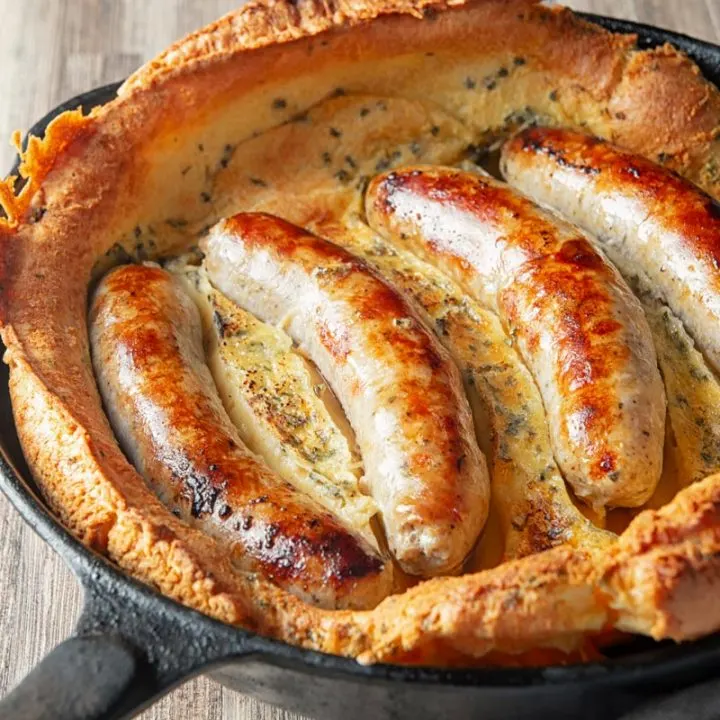 Square close up image of toad in the hole, or sausages cooked in a Yorkshire pudding batter cooked and served in a cast iron skillet