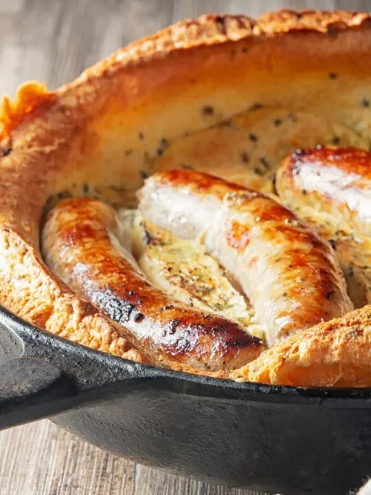 Portrait close up image of toad in the hole, or sausages cooked in a Yorkshire pudding batter cooked and served in a cast iron skillet