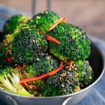 Portrait image of stir fry broccoli featuring sesame seeds, ginger and red pepper served in a mini wok