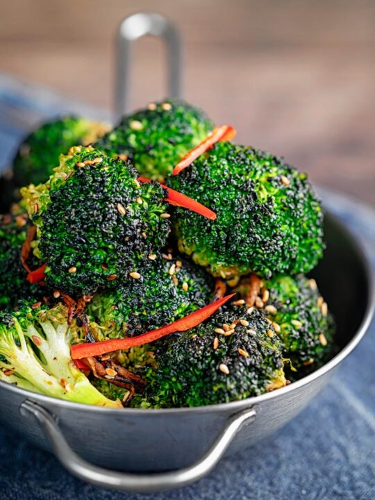 Portrait image of stir fry broccoli featuring sesame seeds, ginger and red pepper served in a mini wok