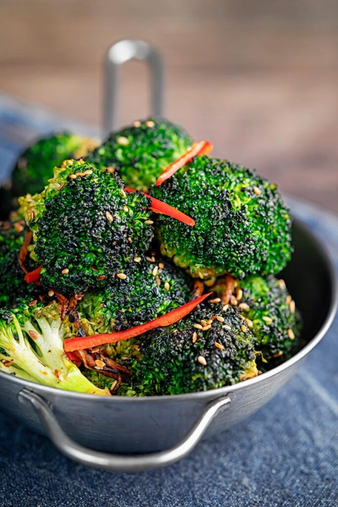 Portrait image of stir fry broccoli featuring sesame seeds, ginger and red pepper served in a mini wok