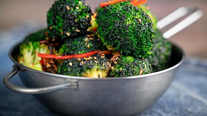 Landscape image of stir fry broccoli featuring sesame seeds, ginger and red pepper served in a mini wok