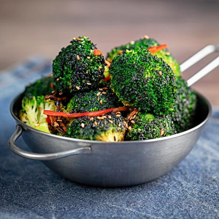 Square image of stir fry broccoli featuring sesame seeds, ginger and red pepper served in a mini wok