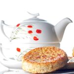 Portrait image of a toasted homemade English crumpet on a white plate in front of a teapot