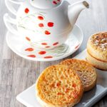 Portrait image of buttered crumpets served on a rectangular white plate with a pot of tea!