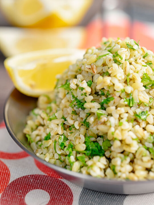 Portrait image of perfectly cooked bulgur wheat with fresh parsley and lemon wedges