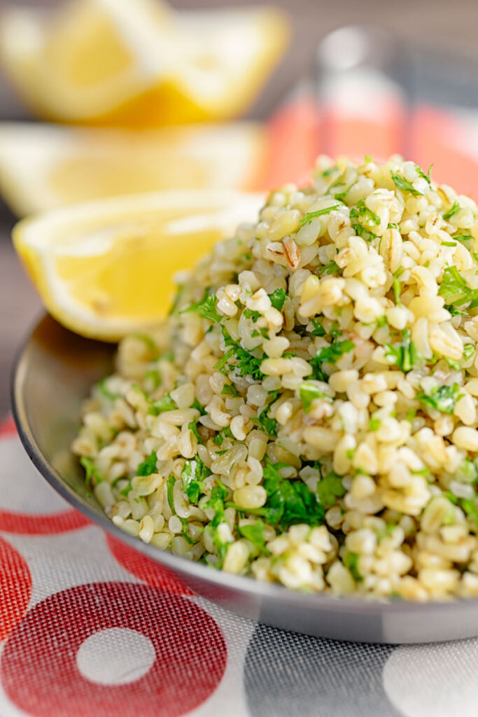 Portrait image of perfectly cooked bulgur wheat with fresh parsley and lemon wedges