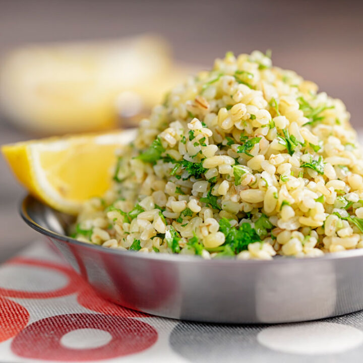 Square image of perfectly cooked bulgur wheat with fresh parsley and lemon wedges