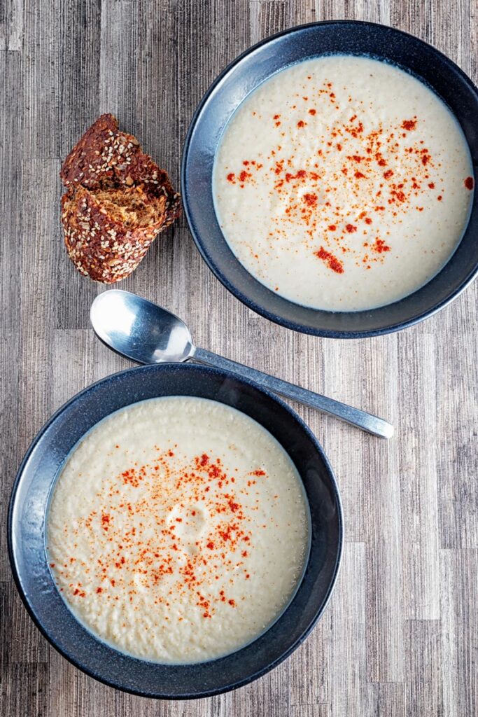 Portrait overhead image of Jerusalem artichoke soup served in a black bowls with a sprinkle of paprika