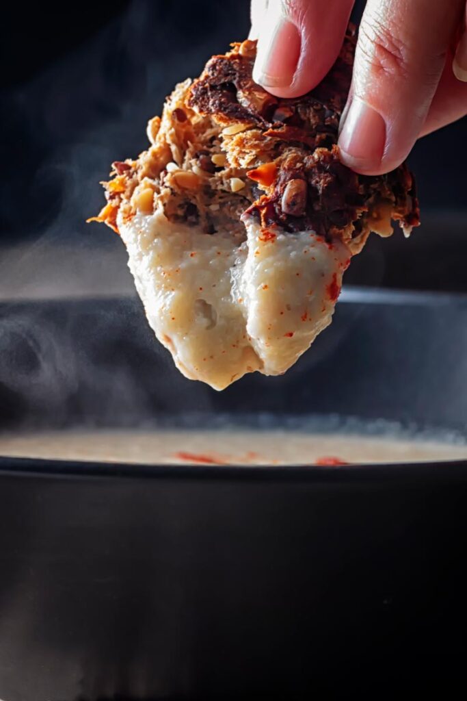 Portrait close up image of a piece of wholegrain bread being dunked into a bowl of Jerusalem artichoke soup