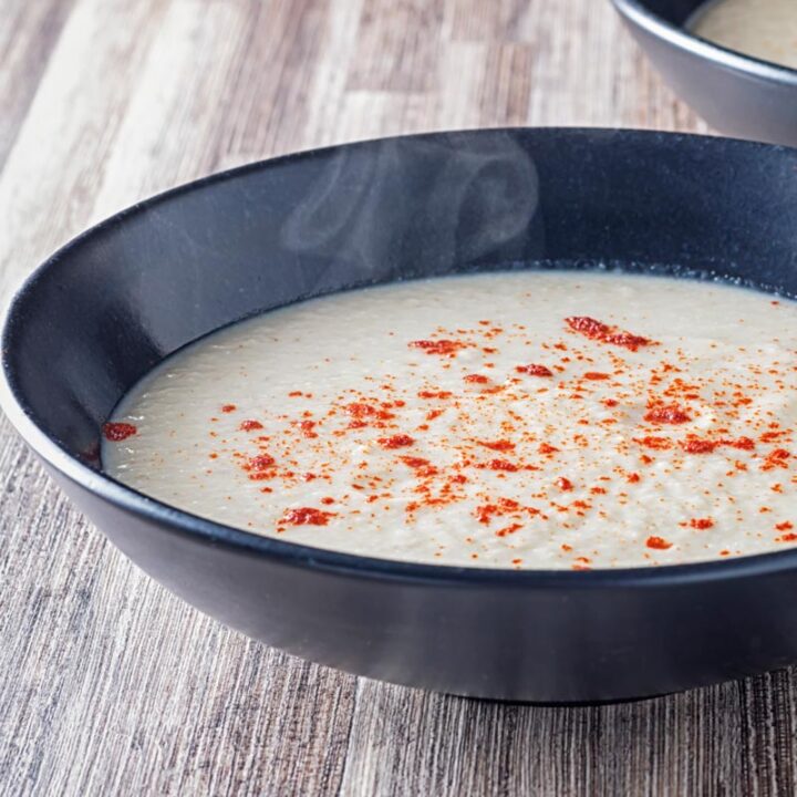 Square image of steaming hot Jerusalem artichoke soup served in a black bowl with a sprinkle of paprika