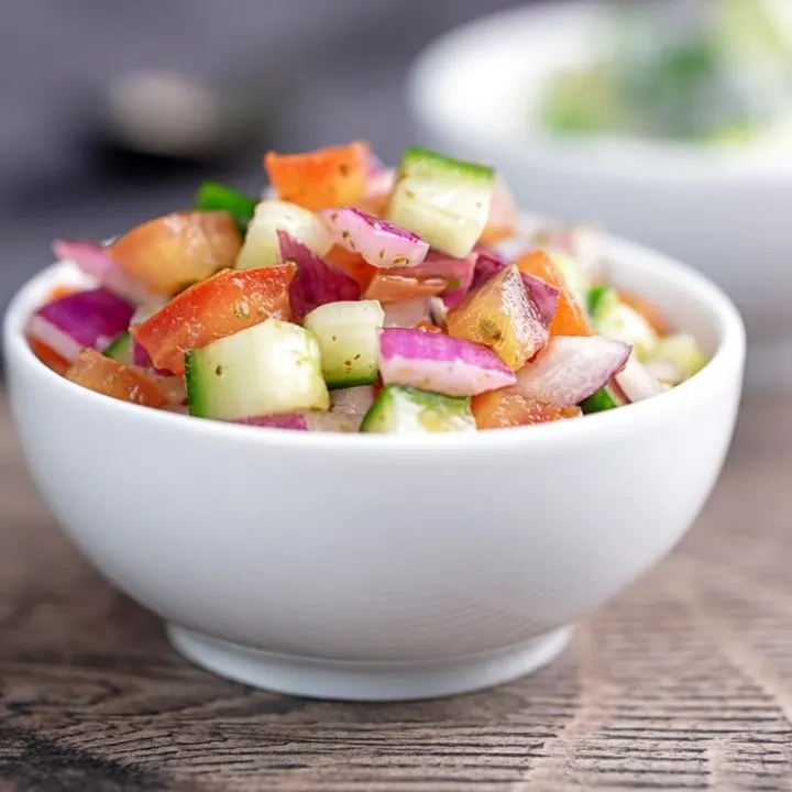 Square image of an Indian kachumber side salad served in a white bowl