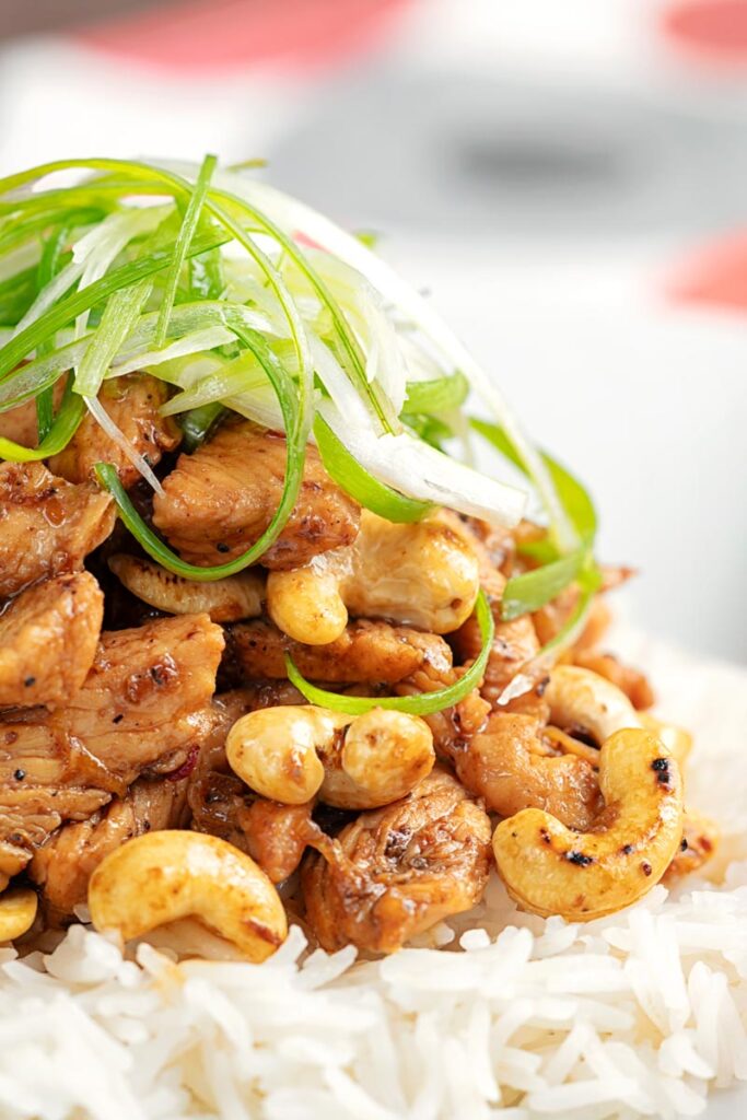 Portrait close up image of kung pao chicken served with rice and shredded spring onions on a white plate