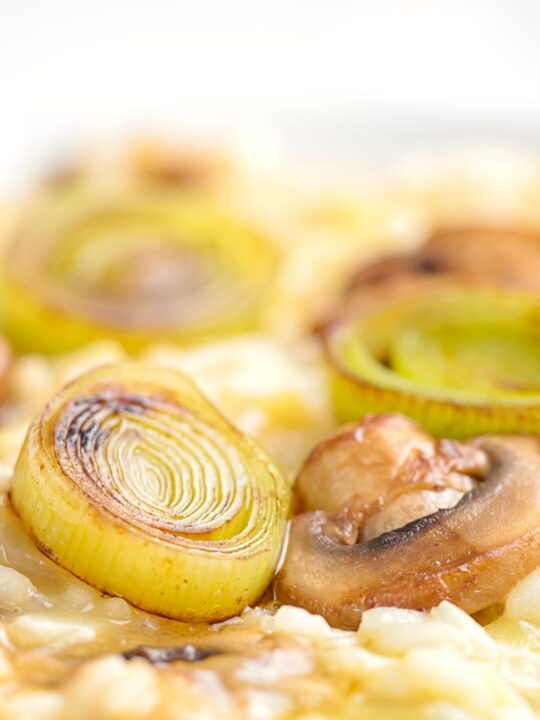 Portrait close up image of a slice of seared leek and mushroom sat on top of a creamy risotto