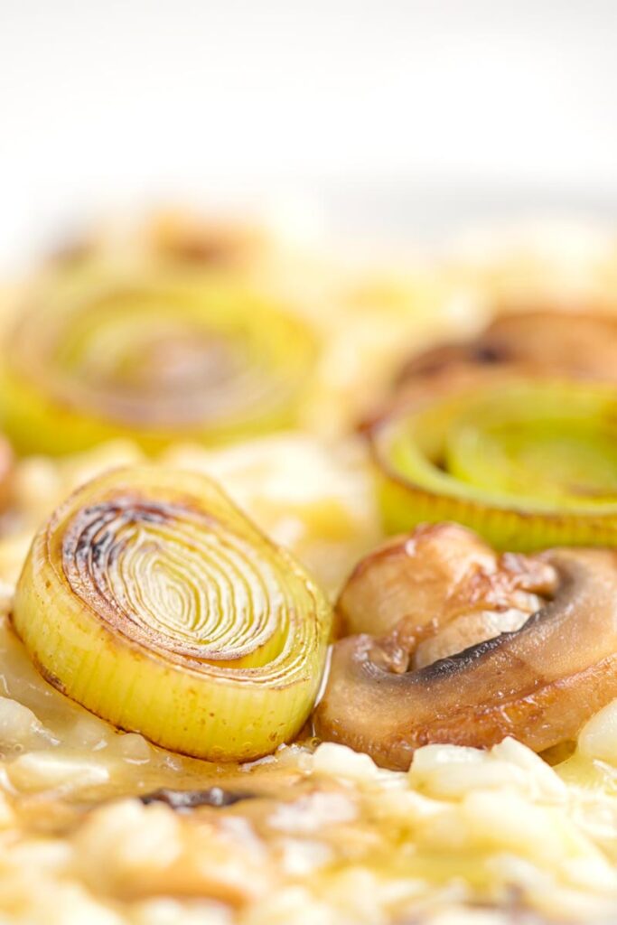 Portrait close up image of a slice of seared leek and mushroom sat on top of a creamy risotto