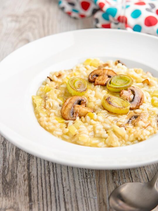 Portrait image of a leek and mushroom risotto served in a white bowl