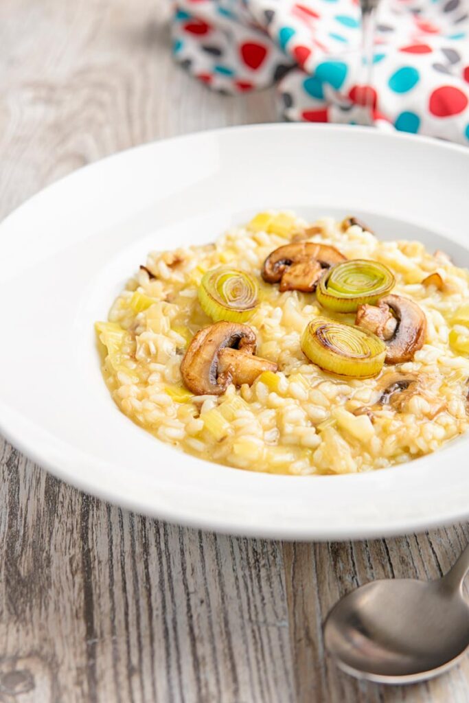 Portrait image of a leek and mushroom risotto served in a white bowl