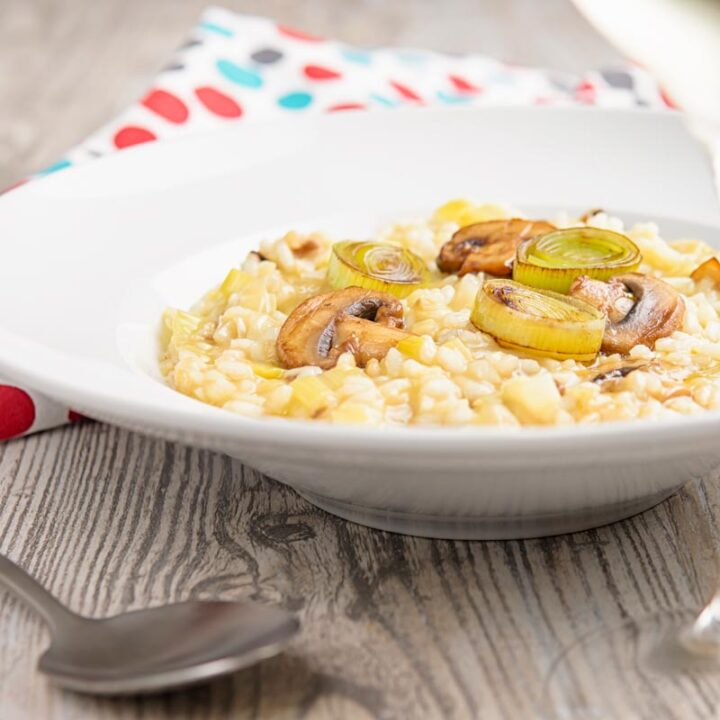 Square image of a leek and mushroom risotto served in a white bowl