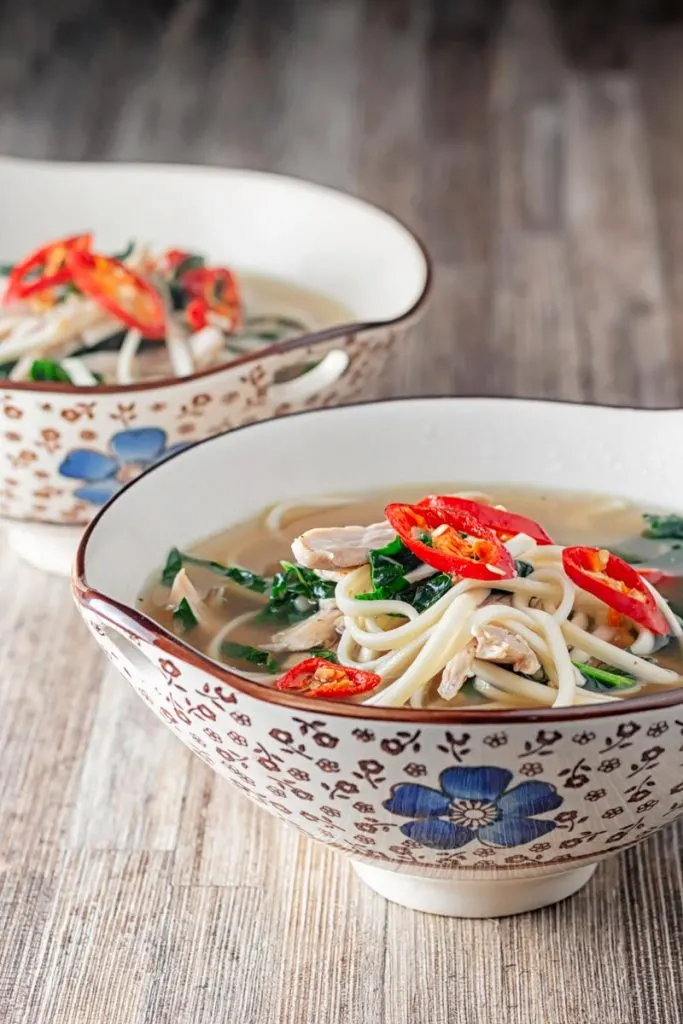 Portrait image of chicken noodle soup made with leftover chicken served in an Asian style bowls decorated with a blue flower