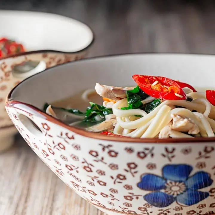 Square close up image of chicken noodle soup made with leftover chicken served in an Asian style bowl decorated with a blue flower