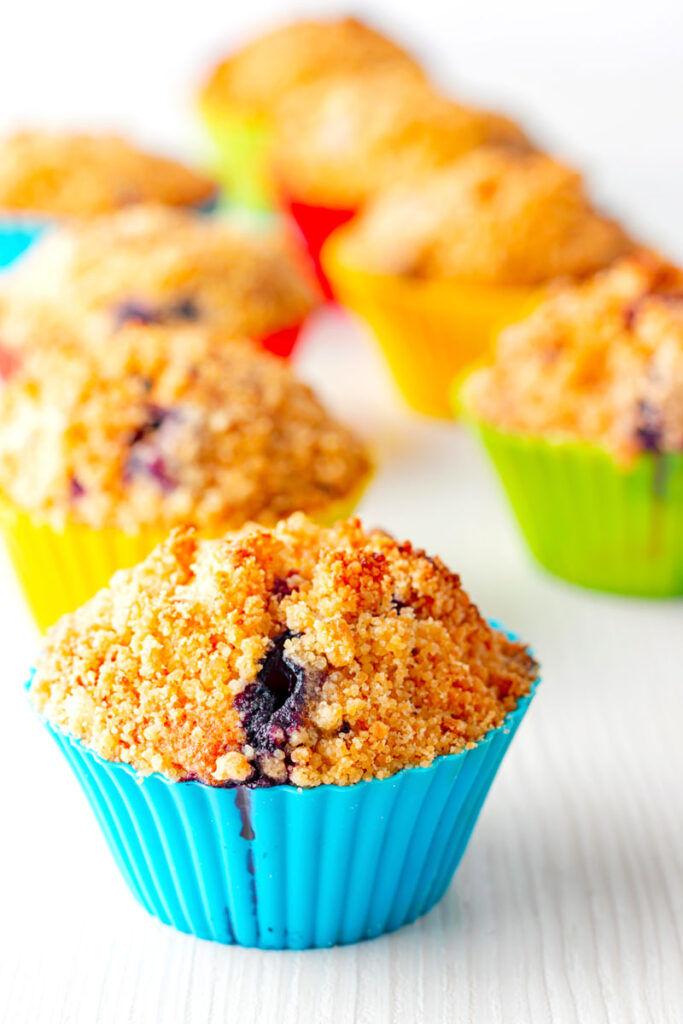 Portrait image of lemon and blueberry muffins in colourful silicon muffin cases on a white backdrop