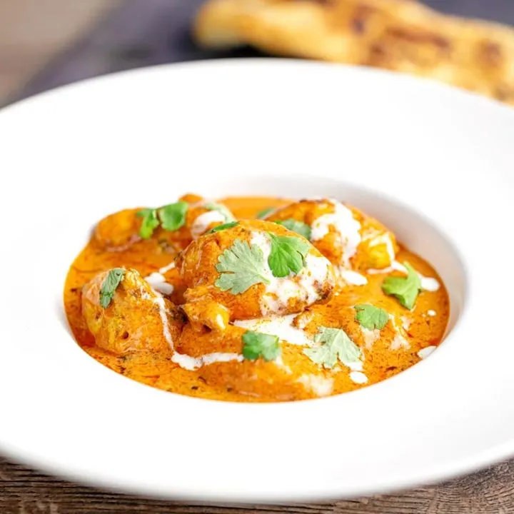 Square image of murgh makhani or a butter chicken curry with a swirl of cream and fresh coriander served in a white bowl
