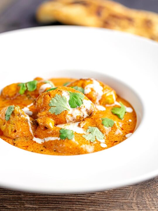 Portrait image of murgh makhani or a butter chicken curry with a swirl of cream and fresh coriander served in a white bowl