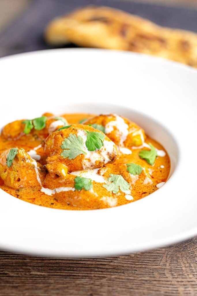Portrait image of murgh makhani or a butter chicken curry with a swirl of cream and fresh coriander served in a white bowl