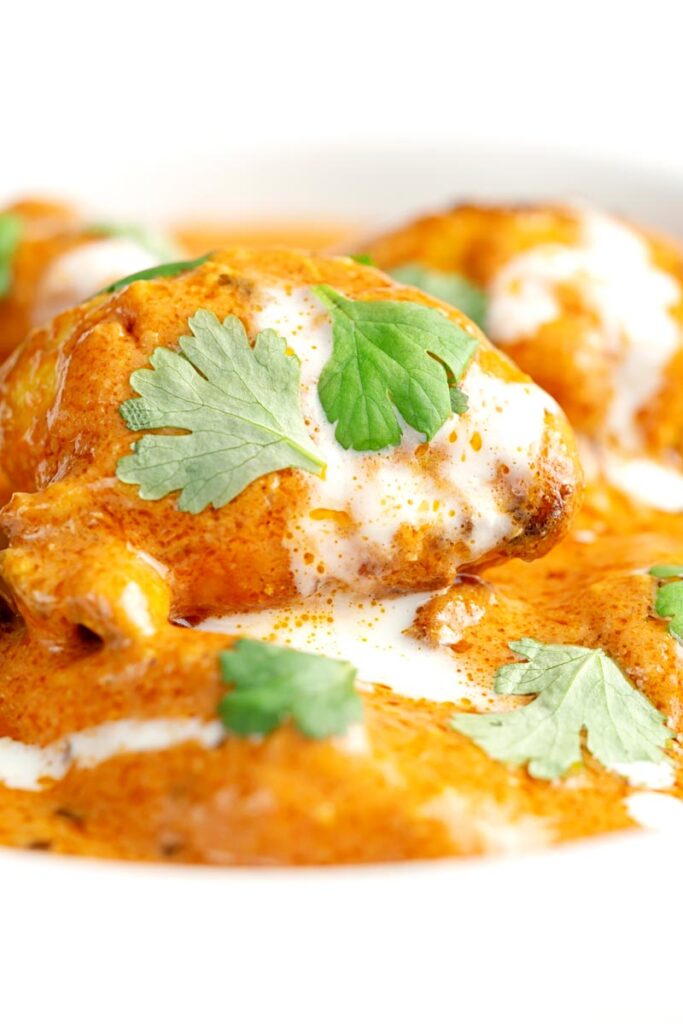 Portrait close up image of murgh makhani or a butter chicken curry with a swirl of cream and fresh coriander